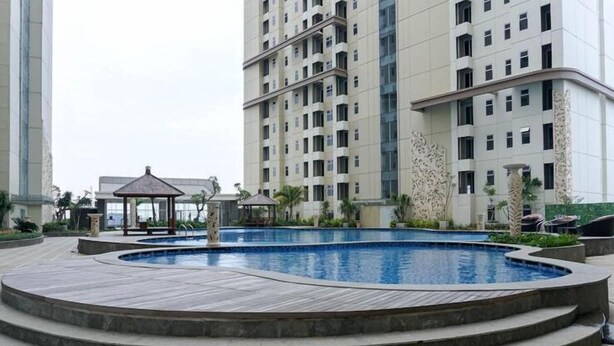 Una piscina rodeada de una terraza de madera, con un pabellón y sillones de descanso al fondo.