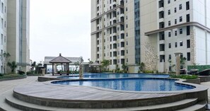 A swimming pool surrounded by a wooden deck, with a gazebo and lounge chairs in the background. - Homey 2BR Apartment with Space Room at Vittoria Residence (Jakarta)