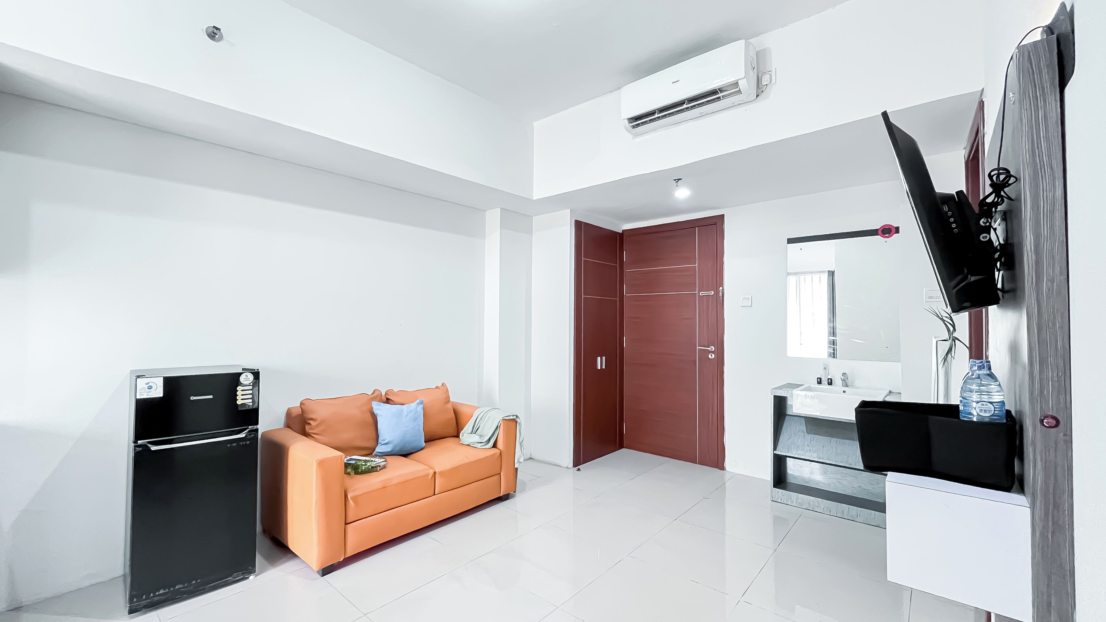 A modern hotel room with a kitchenette, a sofa, a wardrobe, a mirror, and a TV.