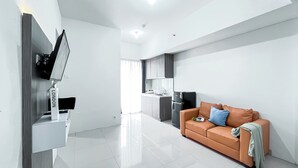 Una sala de estar moderna con un sofá, un televisor de pantalla plana montado en la pared y una zona de cocina al fondo.