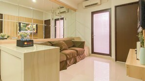 A modern hotel room with a large mirror, a sofa, a small table with a bottle, and a TV on the wall.