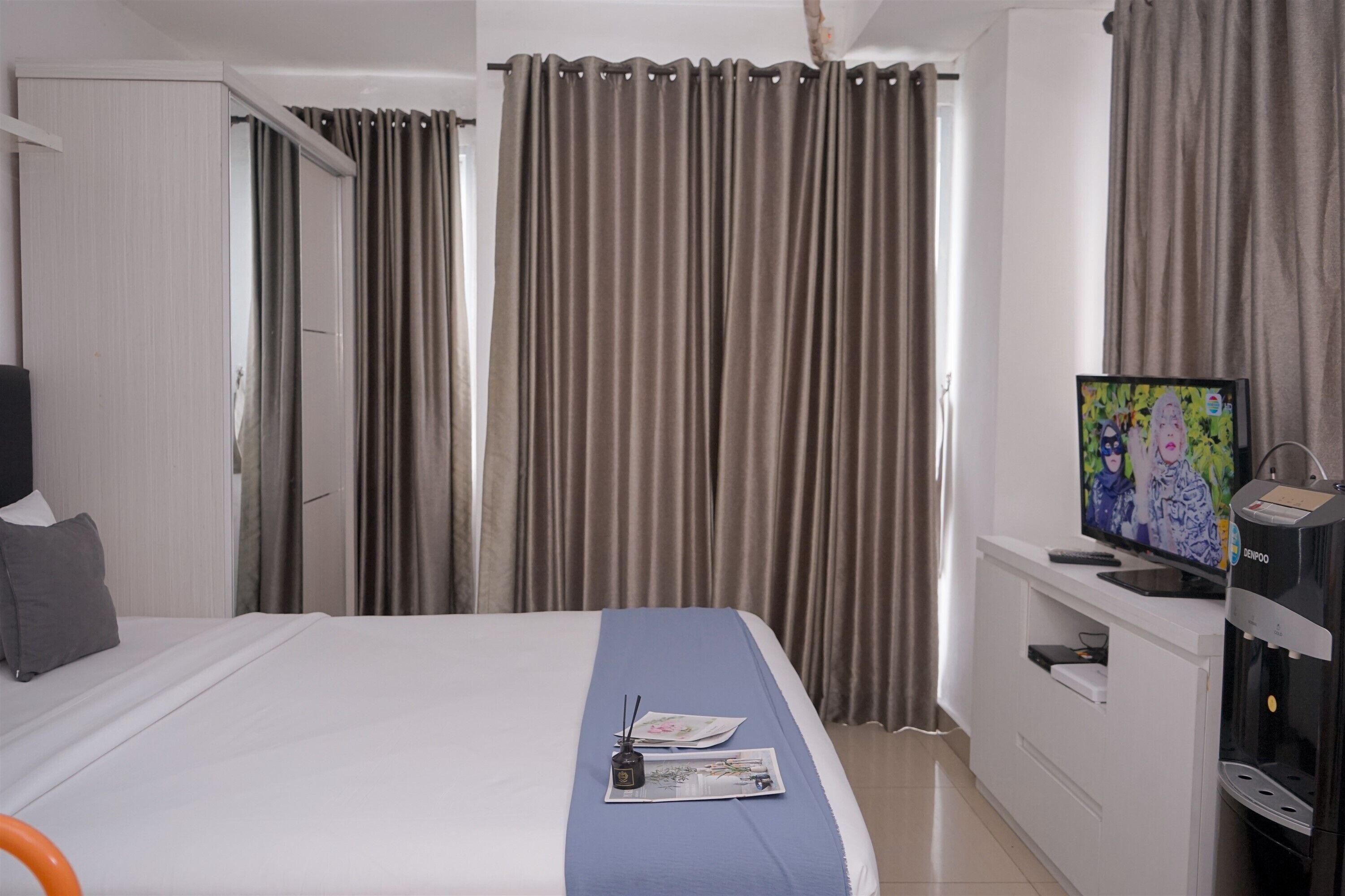 Une chambre d’hôtel avec un lit, une télévision, un minibar et des rideaux.