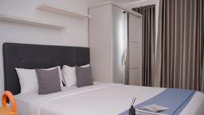 Una cama bien tendida con ropa de cama blanca y gris, un cabecero negro y un detalle azul.