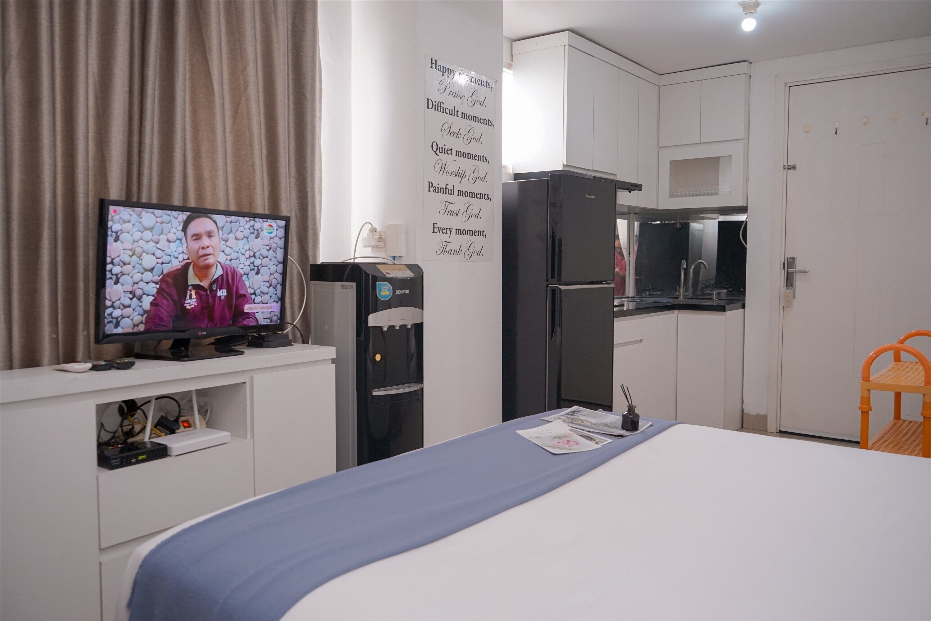 Une chambre d’hôtel équipée d’un lit, d’un téléviseur diffusant une émission, d’un distributeur d’eau, d’un réfrigérateur, d’un four à micro-ondes et d’un évier.