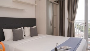 Habitación de hotel con cama, armario, ventana con cortinas y vistas al balcón.