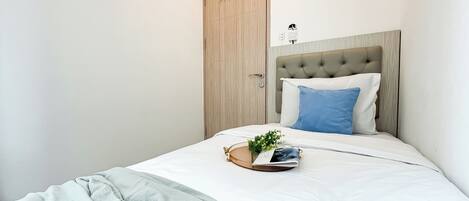 A neatly made bed with a white and blue pillow, a small plant, and a magazine on the bed.