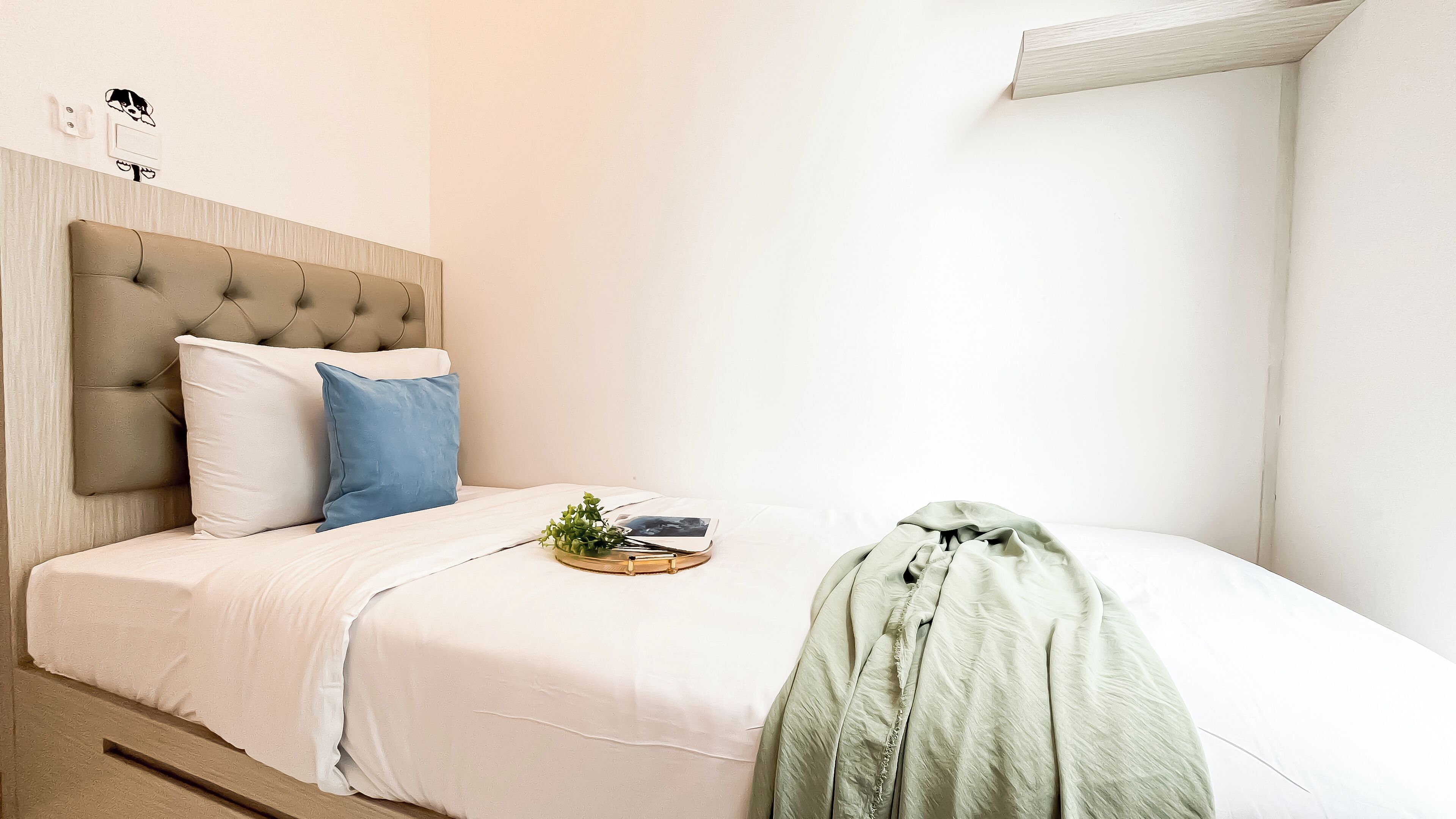 Ein ordentlich bezogenes Bett mit einer weißen Decke, einem blauen Kopfkissen und einer grünen Tagesdecke.
