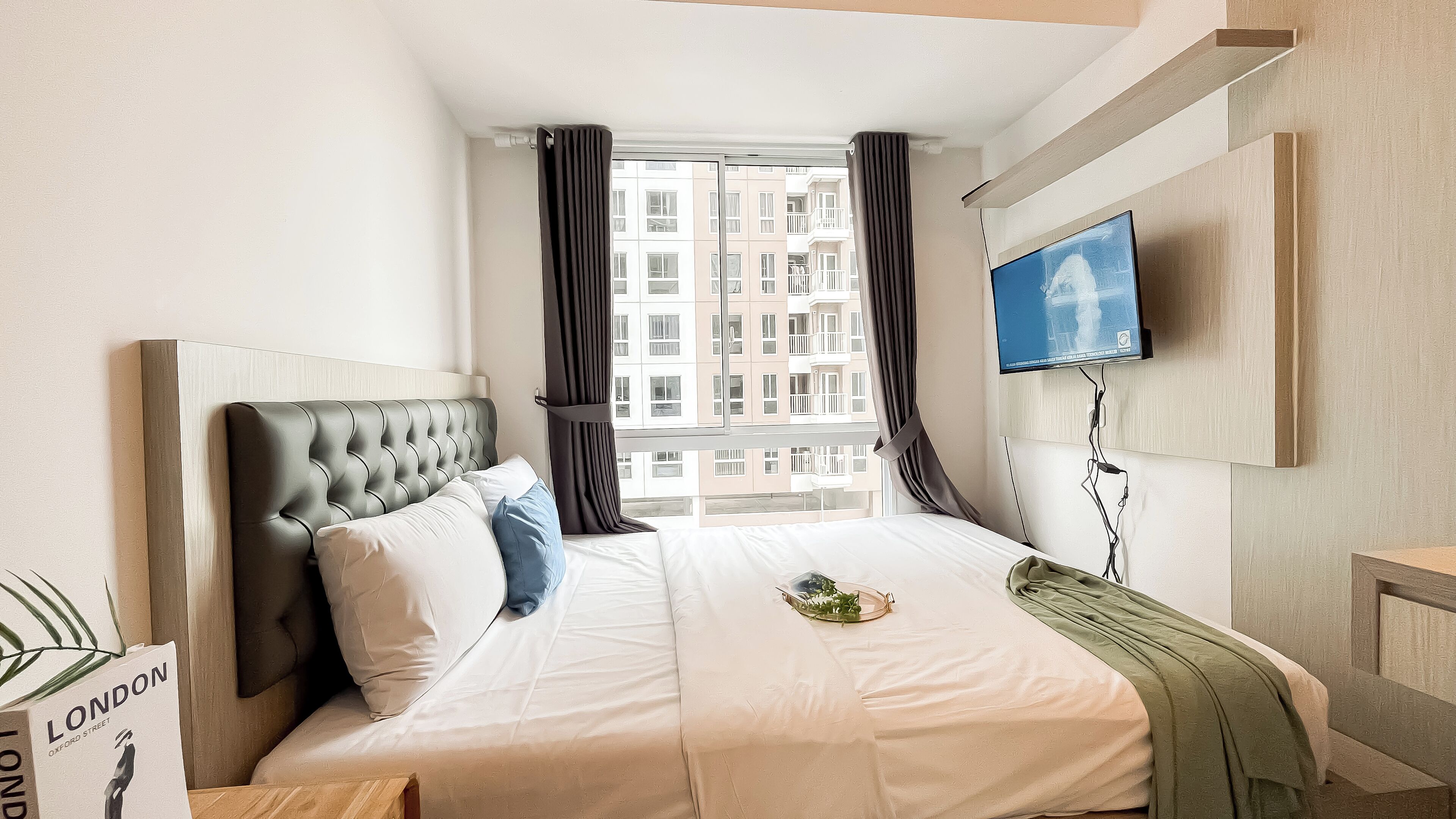 A hotel room with a large bed, a flat-screen TV mounted on the wall, and a view of a building through the window.