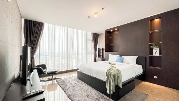 A modern hotel bedroom with a large bed, a TV, a desk, and a view of the city. - Well Designed 1BR Apartment L'Avenue Pancoran (Jakarta)