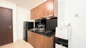 A compact kitchen with wooden cabinets, a black countertop, a stainless steel sink, and a white water dispenser. - Well Designed 1BR Apartment L'Avenue Pancoran (Jakarta)