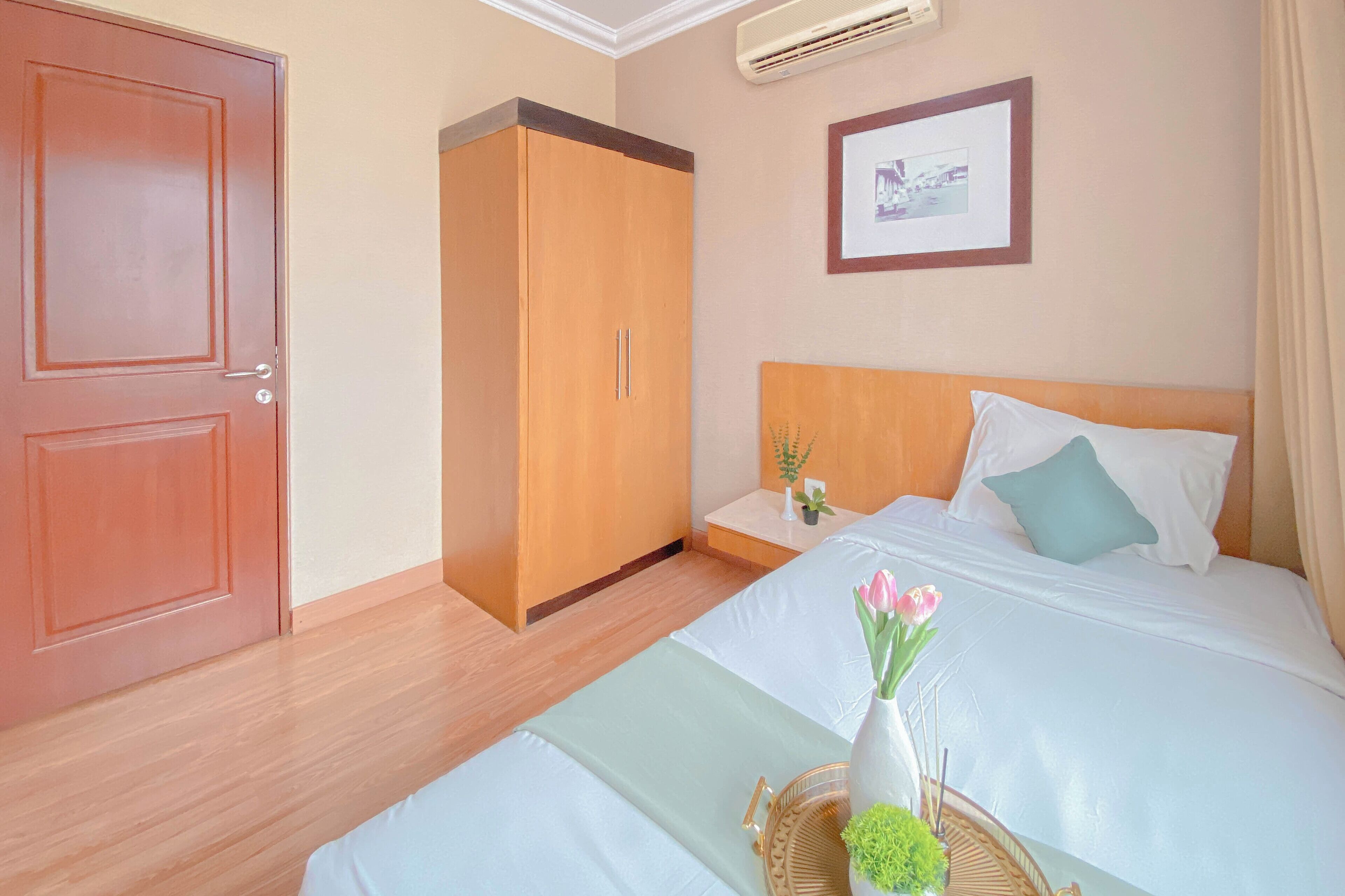 Una habitación de hotel con cama, armario, mesita de noche con planta y un cuadro en la pared.