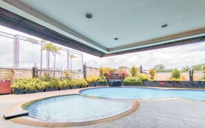 Un espace piscine comprenant deux piscines, dont une avec un jacuzzi, le tout entouré de plantes et d’un mur en pierre.