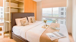 A modern bedroom with a large bed, built-in shelving, and a city view through the window. - Stunning and Well Designed 2BR at Tokyo Riverside PIK 2 Apartment (Teluknaga)