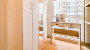 A room with a wooden desk, a bench, and a wardrobe. There is a window with a view of buildings outside. - Stunning and Well Designed 2BR at Tokyo Riverside PIK 2 Apartment (Teluknaga)