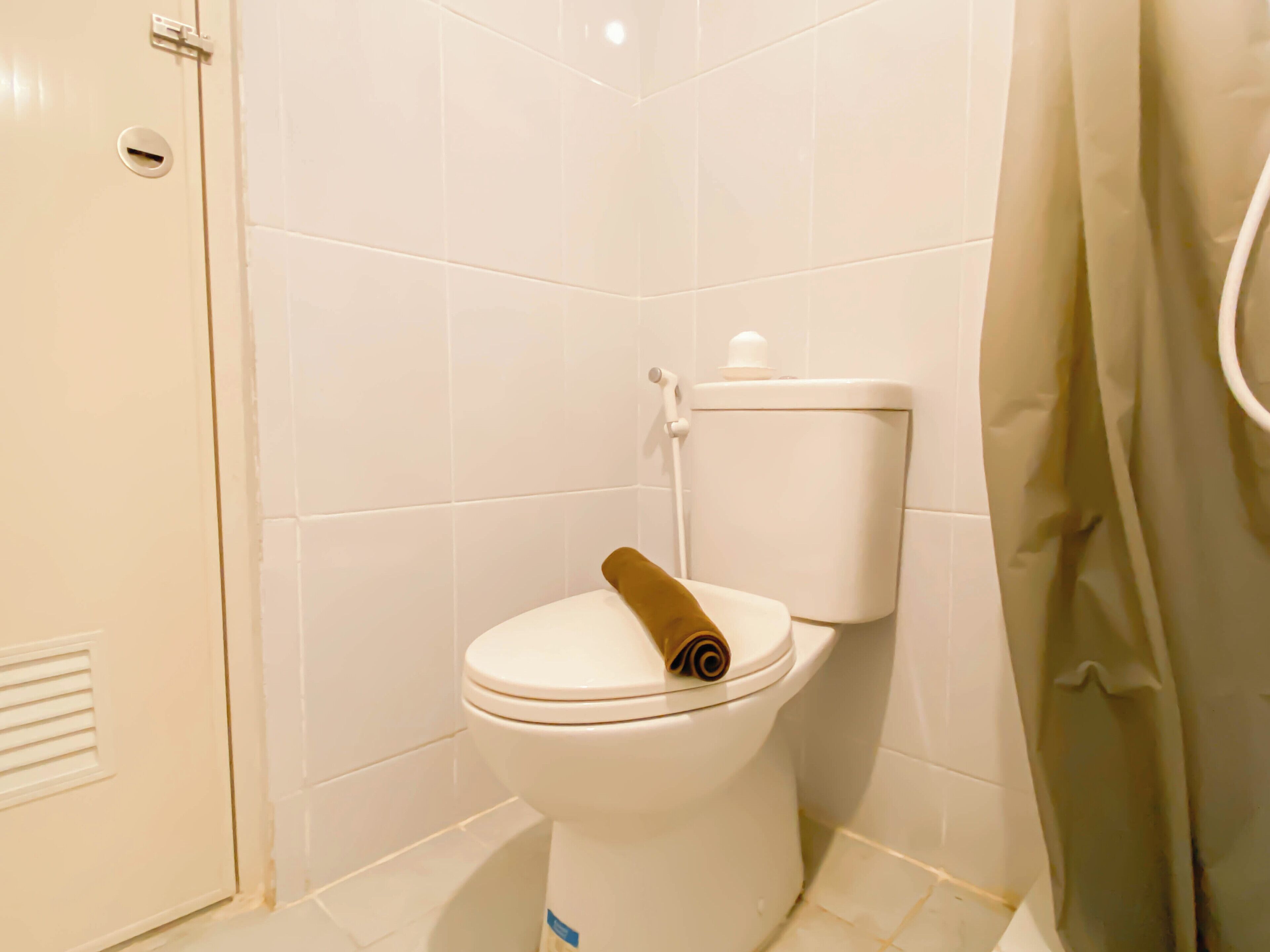 A white toilet with a brown toilet paper holder in a bathroom with white tiles.