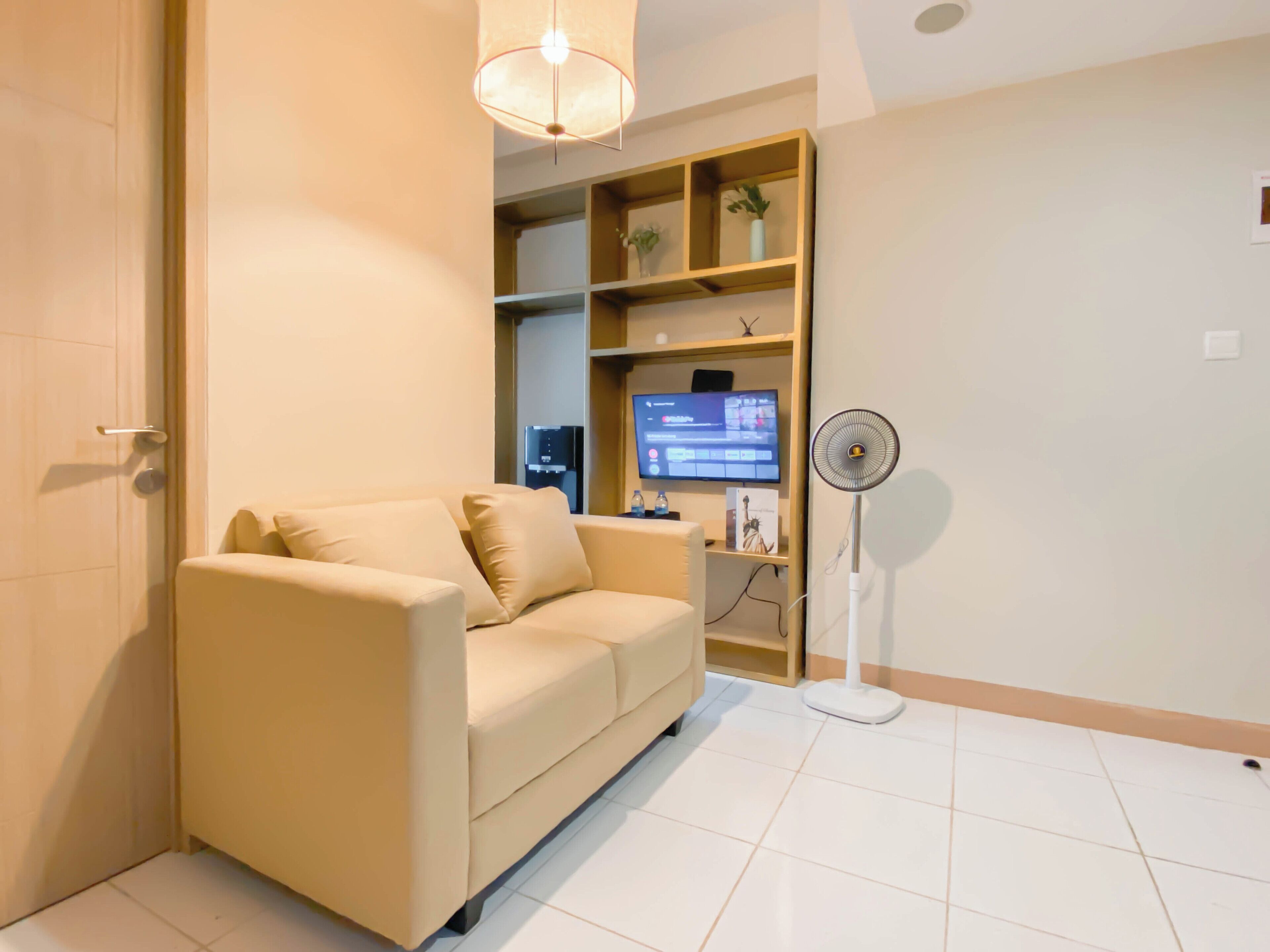 Ein modernes Wohnzimmer mit einem beige farbenen Sofa, einem Flachbildfernseher, einem Standventilator und einer Holzhängeregalschrank.