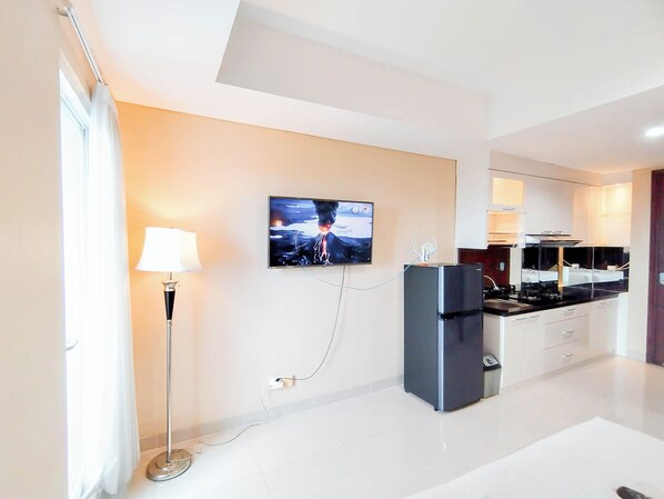 A modern kitchen with a flat-screen TV mounted on the wall, a refrigerator, and a dining area with a table and chairs.