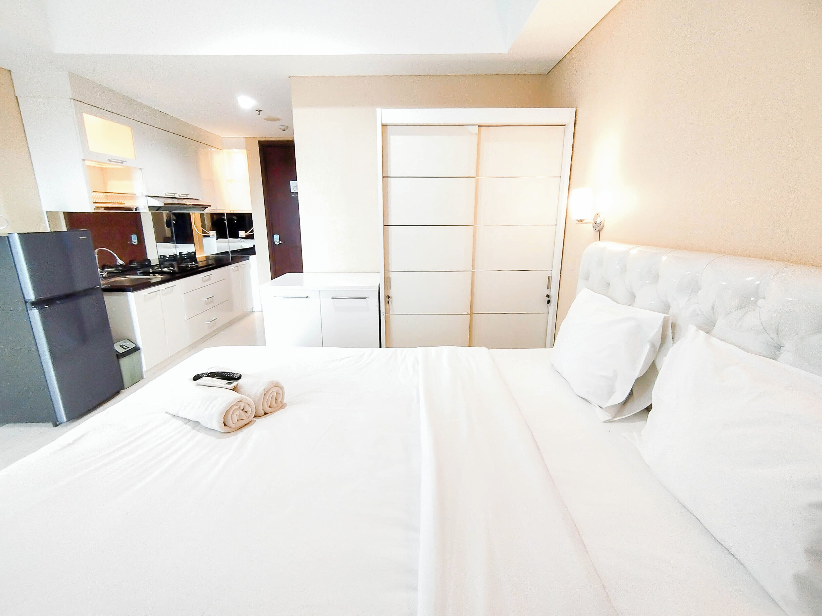 A hotel room with a bed, a refrigerator, a kitchen area, and a wardrobe.