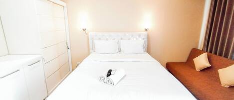 A hotel room with a bed, a nightstand, a wardrobe, and a brown sofa.