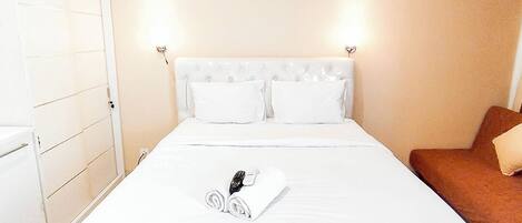 A hotel room with a bed, a brown chair, and a white wardrobe.
