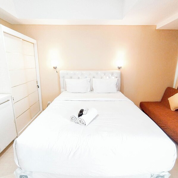 A hotel room with a bed, a brown chair, and a white wardrobe.