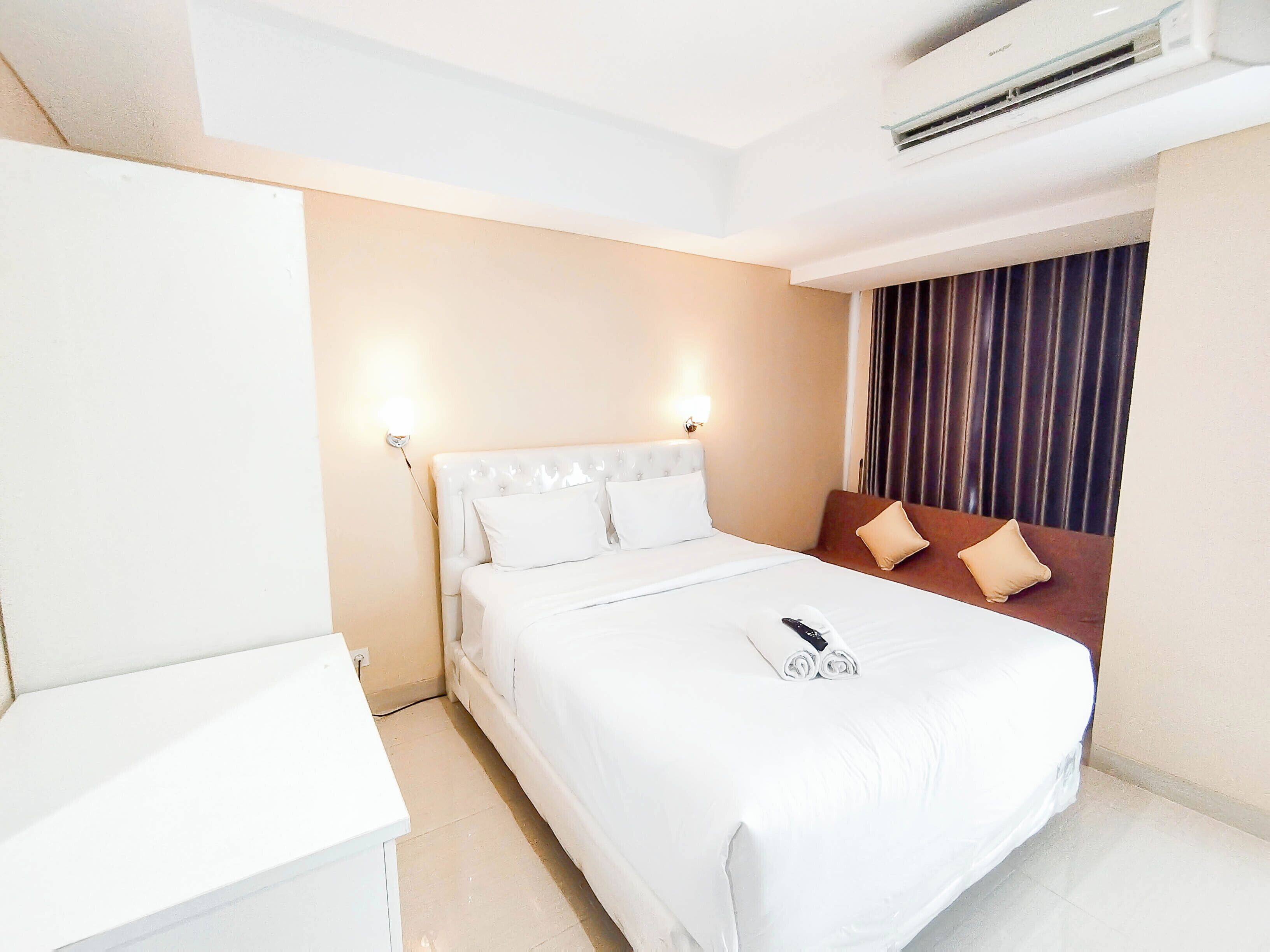 A hotel room with a bed, a bedside table, a lamp, and an air conditioning unit.