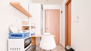 Une cuisine compacte équipée d’un four à micro-ondes, d’un grille-pain et d’un petit réfrigérateur. On y trouve une chaise blanche et une poubelle.