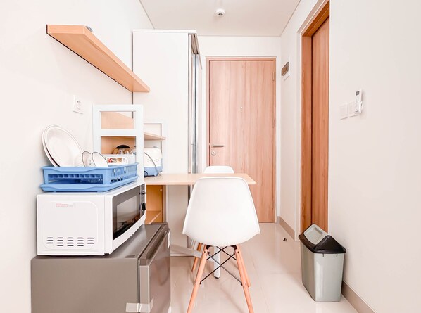 A compact kitchen with a microwave, toaster, and a small fridge. There is a white chair and a trash bin. - Comfortable Studio Room (No Kitchen) at Bandaraya - Tallasa City Makassar Apartment (Makassar)