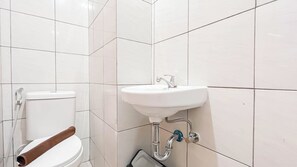 Un bagno con piastrelle bianche, un lavandino bianco e un WC con portasciugamani marrone.