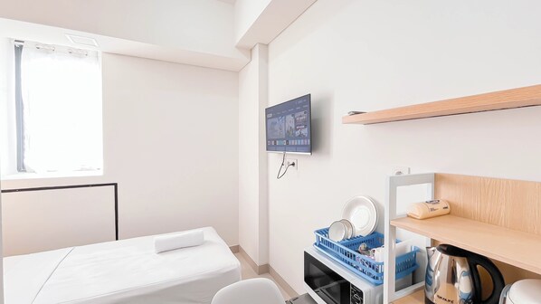Una moderna camera d'albergo con un letto, una televisione montata a parete, un angolo cottura con un bollitore e una finestra con tende.