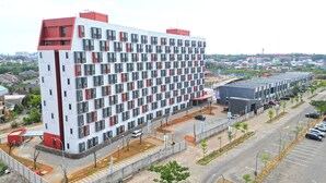 Un hôtel à plusieurs étages, doté d’un design moderne, avec une façade uniforme ponctuée de nombreuses fenêtres et un élément décoratif rouge sur le toit.