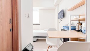 Une chambre d’hôtel équipée d’un lit, d’un bureau avec un ordinateur, d’une télévision et d’une étagère contenant des appareils de cuisine.