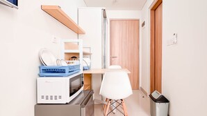 Une cuisine compacte équipée d’un four à micro-ondes, d’un grille-pain et d’un petit réfrigérateur. On y trouve une chaise blanche et une poubelle.