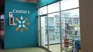 Eine Apotheke namens 'Century' mit einer türkisfarbenen Wand und einem Logo, das eine stilisierte Sonne zeigt.