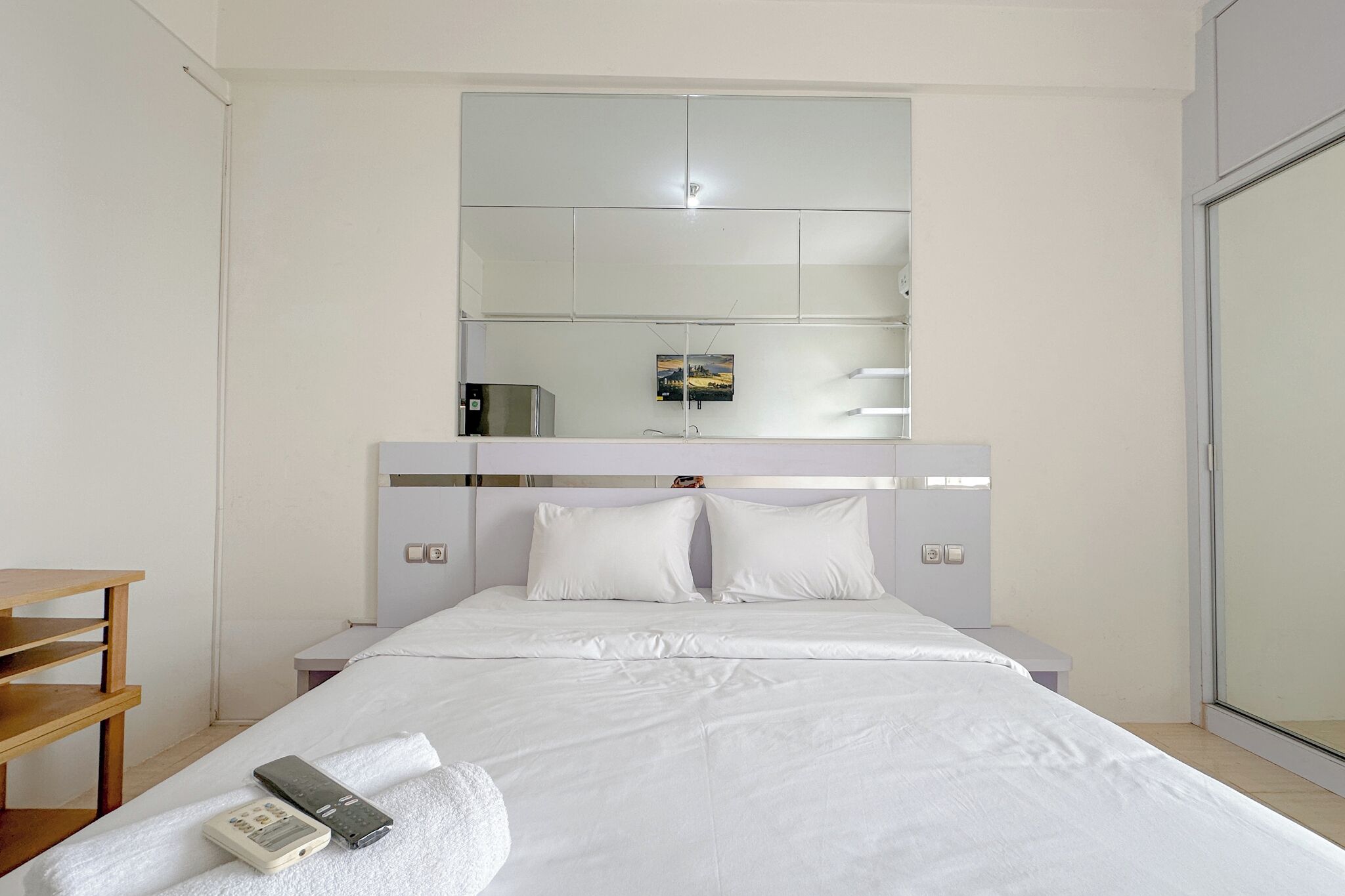 Een hotelkamer met een groot bed, een nachtkastje, een klein bureau en een grote spiegel boven het bed.