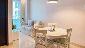 A modern living room with a round dining table, white chairs, a sofa, and a large window with curtains.