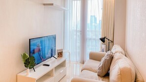 A modern living room with a flat-screen TV, a white console table, a beige sofa, and sheer curtains.