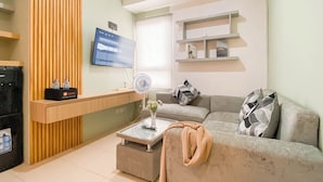 Ein modernes Wohnzimmer mit Flachbildfernseher an der Wand, einer Couch mit dekorativen Kissen, einem Glastisch und einem hölzernen Empfangsbereich.