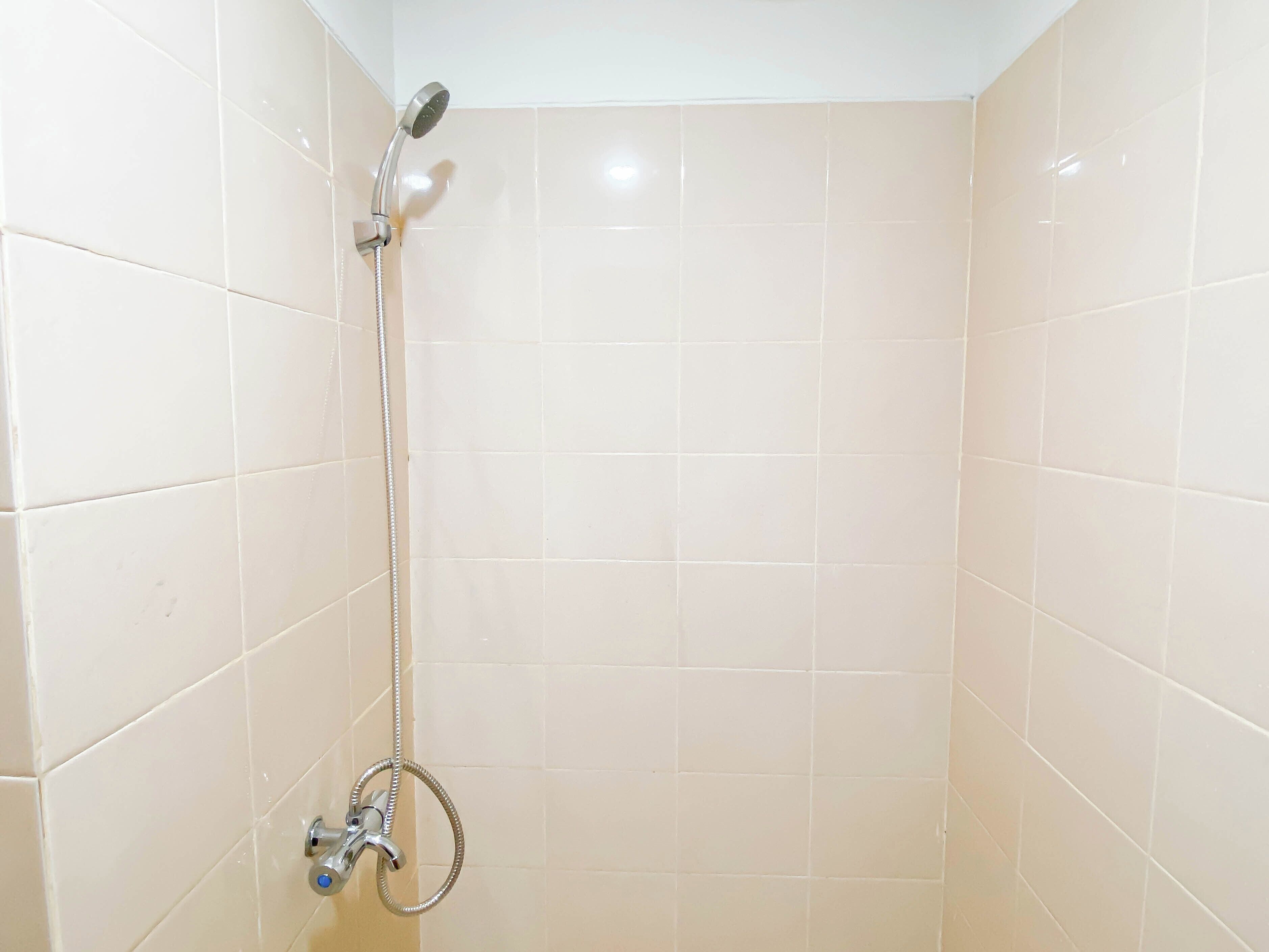 A small, tiled shower area with a handheld showerhead and a wall-mounted faucet.