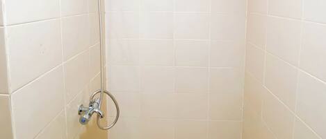 A small, tiled shower area with a handheld showerhead and a wall-mounted faucet.