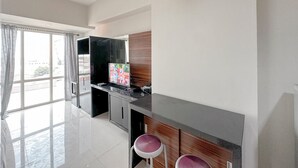 A modern kitchen with a black countertop, wooden cabinets, and a large window with curtains. - Minimalist and Cozy Studio at The Square Surabaya Apartment (Surabaya)