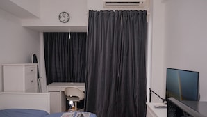 A hotel room with a bed, a desk, a computer, a TV, and a window with curtains. - Warm Studio Apartment M-Town Residence (Gading Serpong)