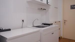 A modern kitchen with white cabinetry, a stainless steel sink, and a black countertop. - Warm Studio Apartment M-Town Residence (Gading Serpong)