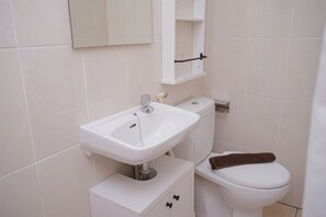 Une salle de bain avec un lavabo, des toilettes et un meuble de rangement, le tout de couleur blanche.