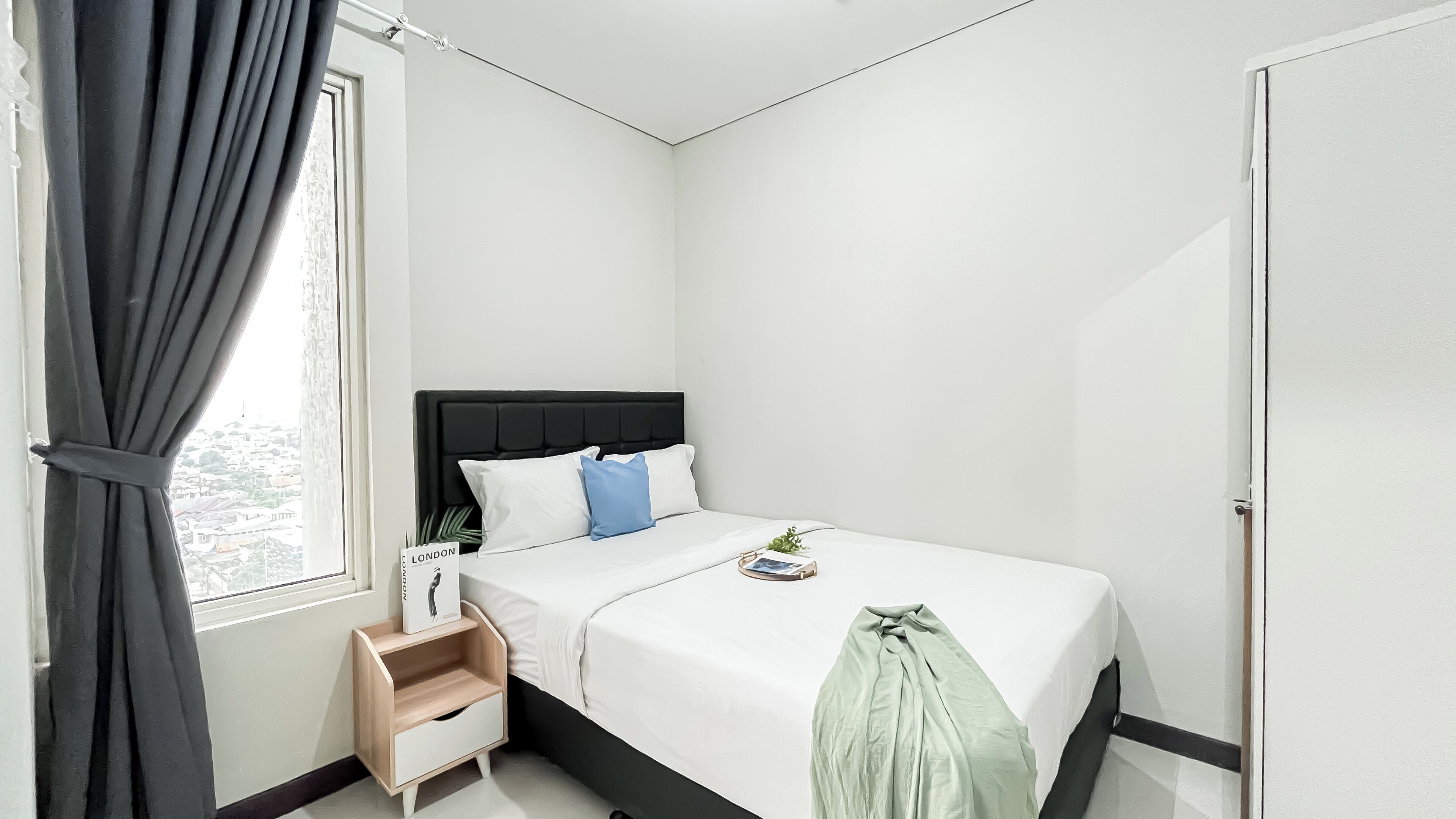A minimalist bedroom with a bed, a nightstand, a window with curtains, and a view of the city.
