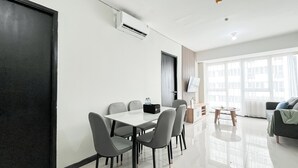 A modern living room with a dining area, large windows, and a flat-screen TV. - Well Designed and Comfortable 3BR Nifarro Park Apartment (Jakarta)