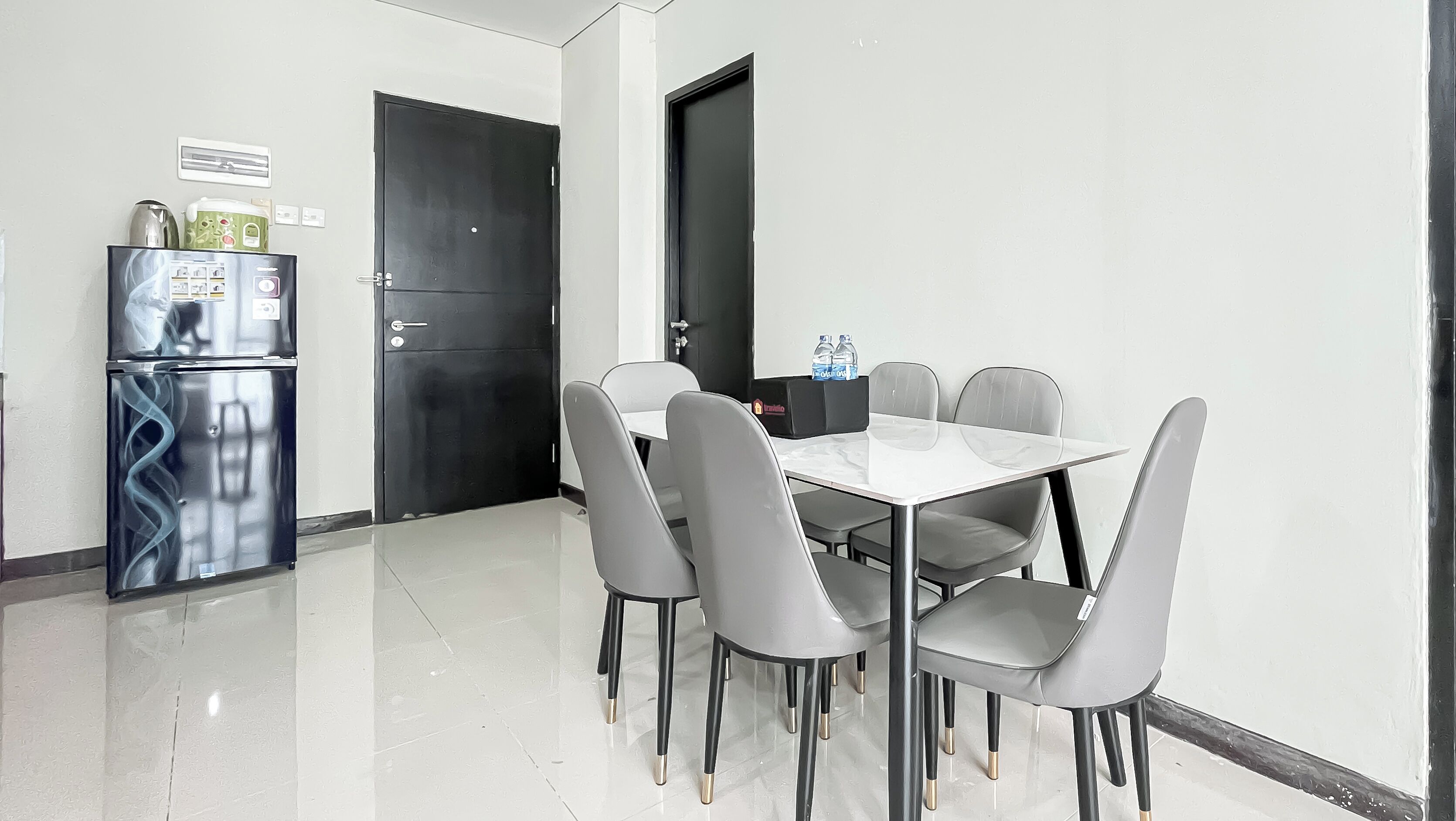 Un comedor moderno con una mesa blanca y sillas grises, un refrigerador negro y una puerta negra.