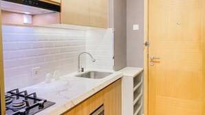 A kitchen with white subway tiles, a stainless steel sink, a gas stove, and wooden cabinets. - Spacious Studio Apartment at Capitol Suites (Jakarta)