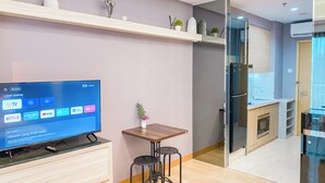 A modern living room with a flat-screen TV, a wooden table, two black stools, and a small potted plant. - Spacious Studio Apartment at Capitol Suites (Jakarta)