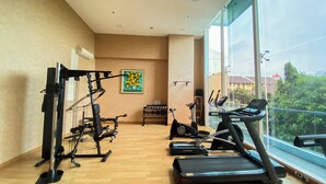 A gym with exercise equipment, a treadmill, and a window with a view of buildings and trees. - Spacious Studio Apartment at Capitol Suites (Jakarta)